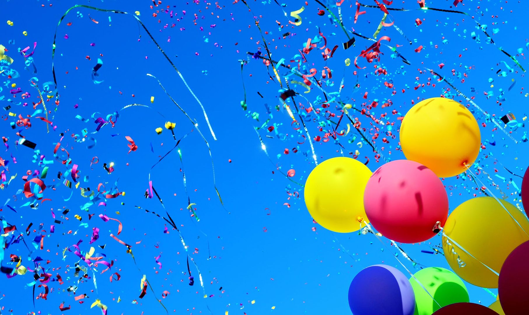 Bunte Luftballons und Konfetti vor einem strahlend blauen Himmel.