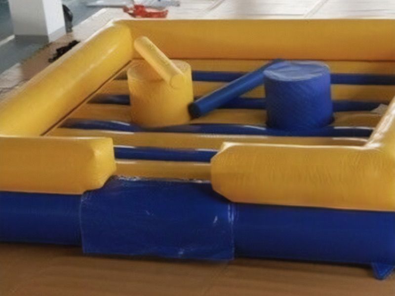 Aufblasbare gelb-blaue Gladiator-Arena mit runden Plattformen und Schaumstoff-Polstern, die für ein spielerisches Duell genutzt werden können.