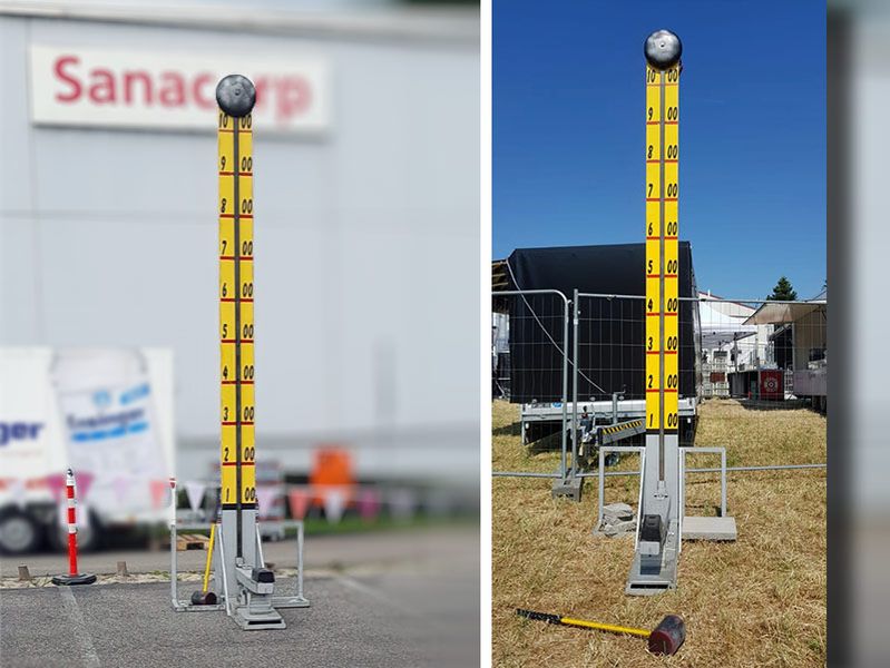 Hau den Lukas, bei dem mit einem Hammer auf eine Platte geschlagen wird, um einen Gewichtsschlitten eine senkrechte Skala hochzuschlagen. Die Skala ist gelb mit schwarzen Zahlen, oben befindet sich jeweils eine silberne Glocke. Die Geräte stehen im Freien auf Asphalt und Wiese.